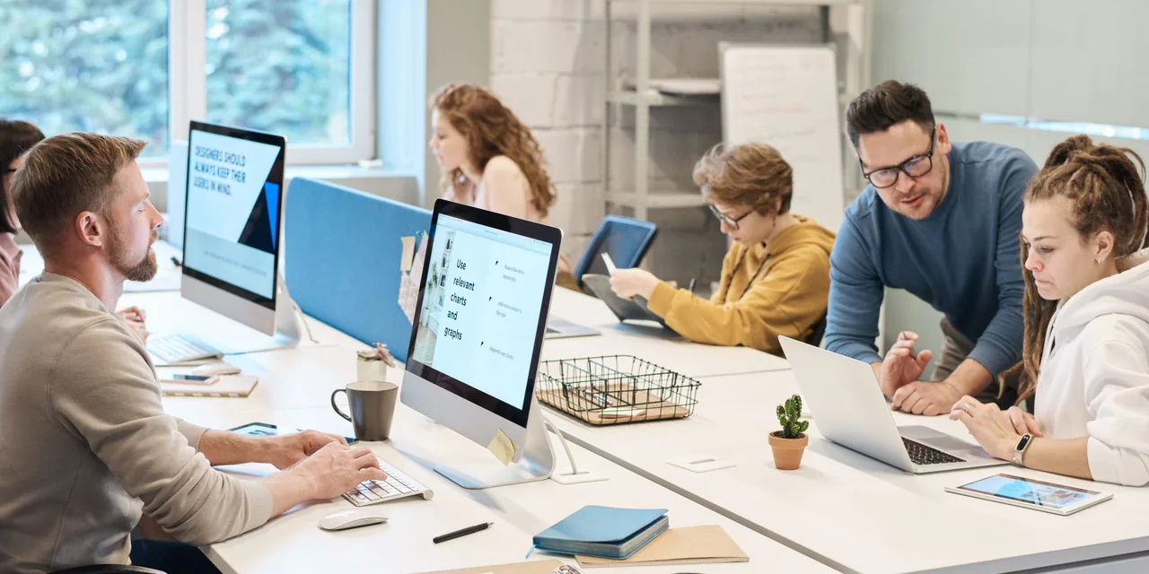 Equipe trabalhando com computadores em um escritório compartilhado e iluminado.