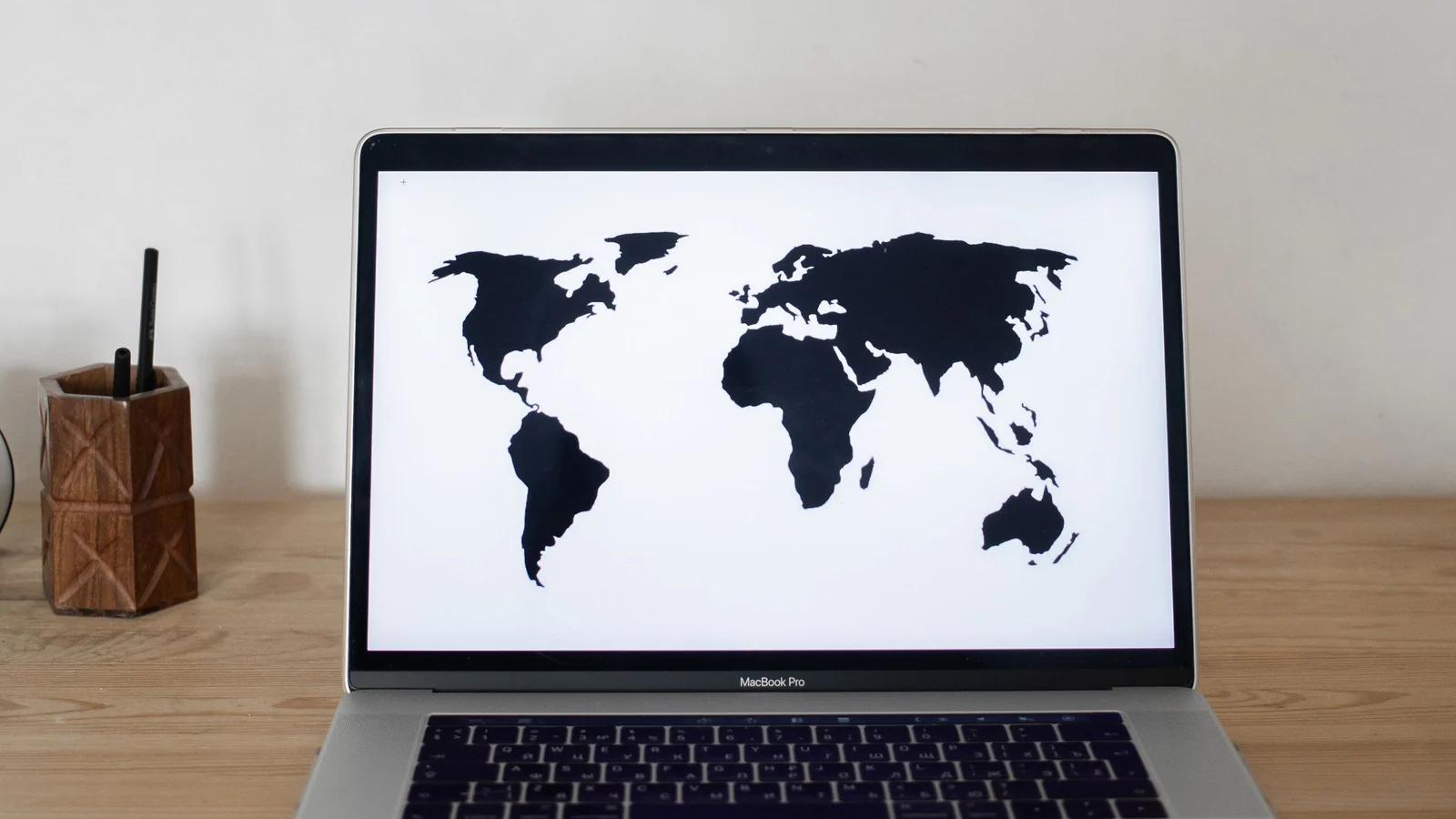 Notebook aberto exibe um mapa-múndi diante de um mapa de cortiça na parede.