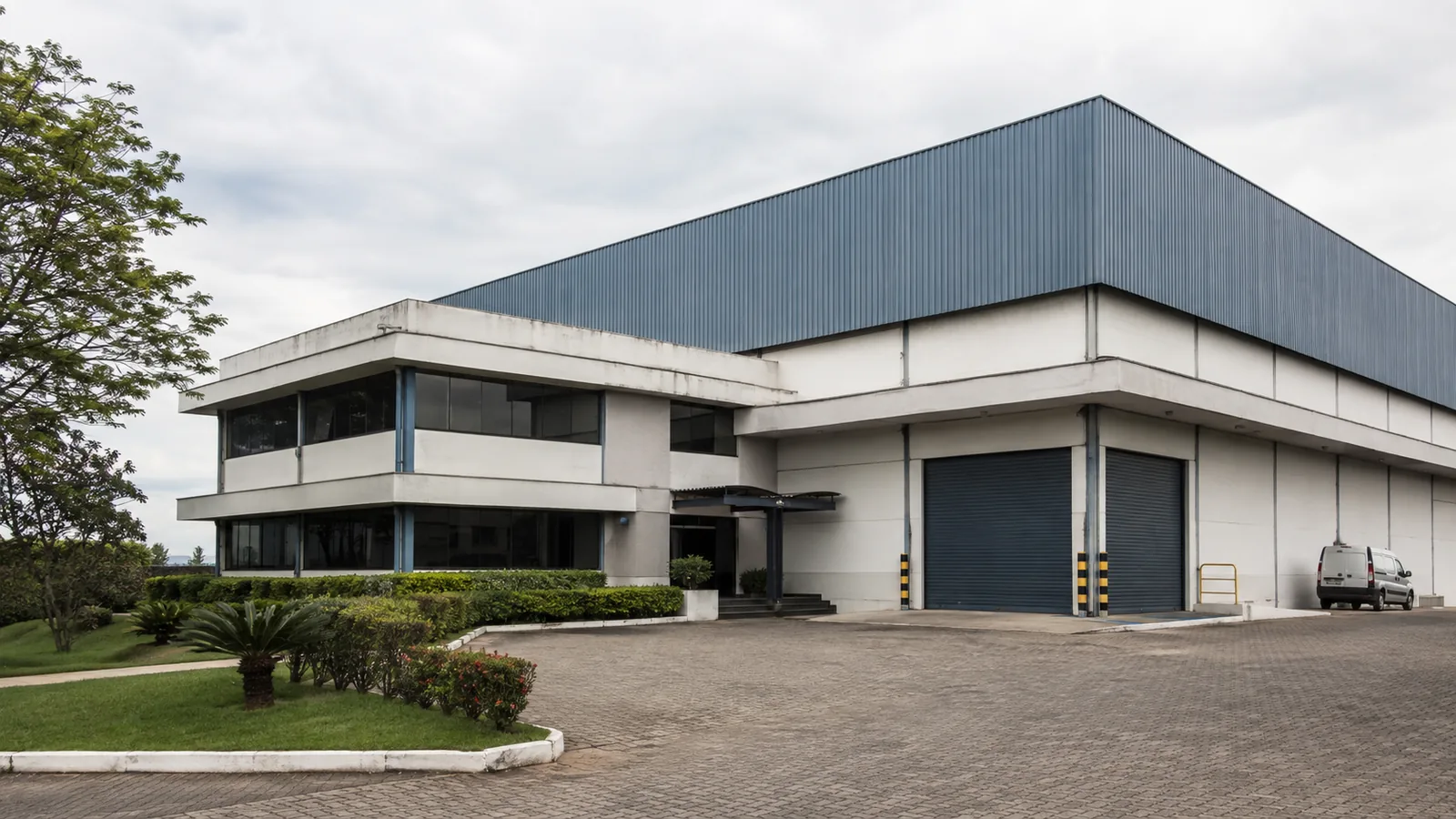 Instalação empresarial vista em perspectiva com atividade operacional ao fundo.